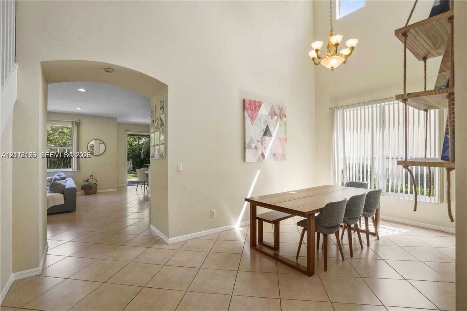 Two-story vaulted ceiling featuring a multi-arm chandelier and arched architectural opening with ceramic tile flooring Two-story vaulted ceiling featuring a multi-arm chandelier and arched architectural opening with ceramic tile flooring