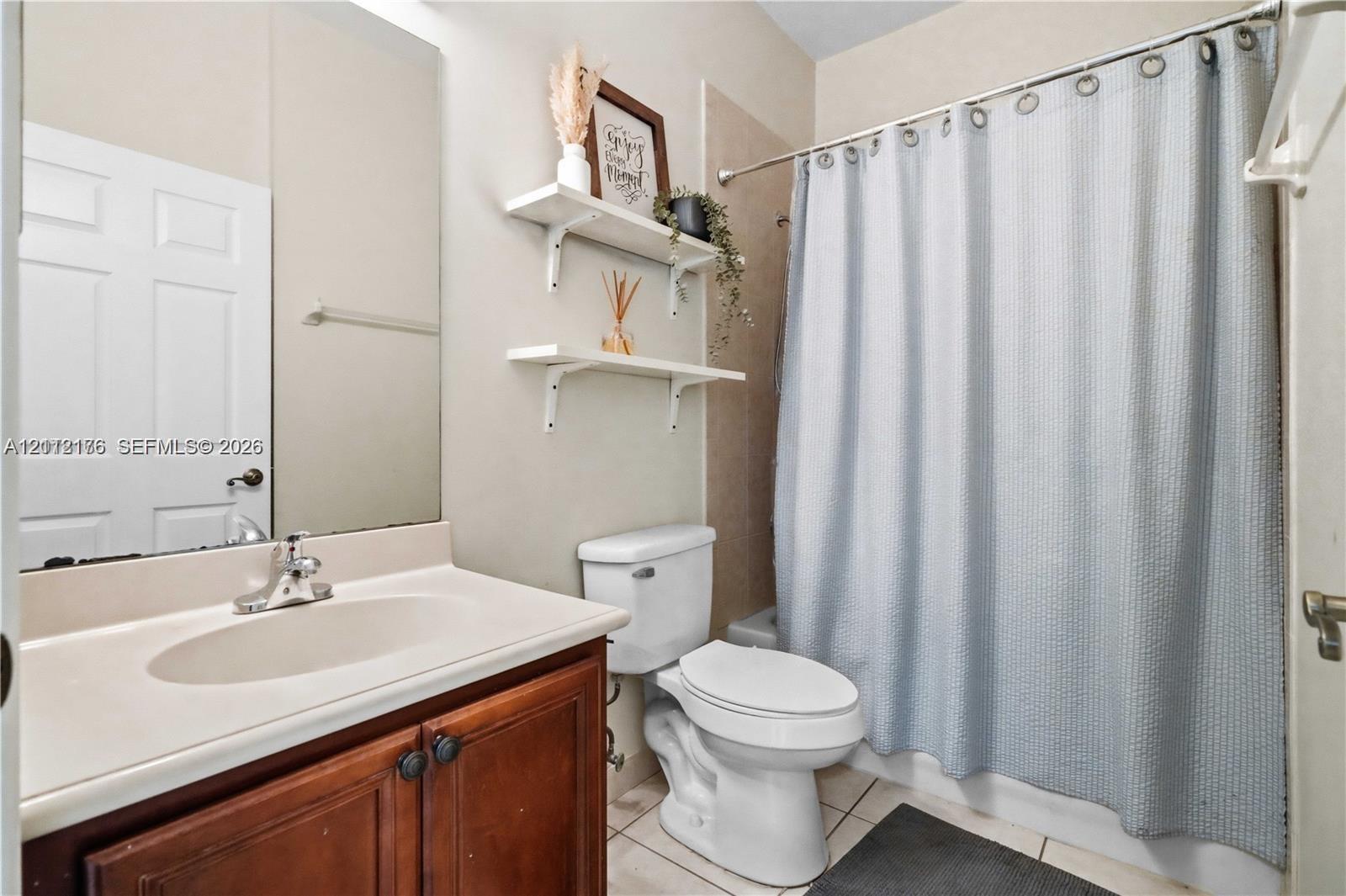 Bathroom featuring a wood-finish vanity with an integrated oval sink, full-width wall mirror, tile flooring, and wall-mounted shelving