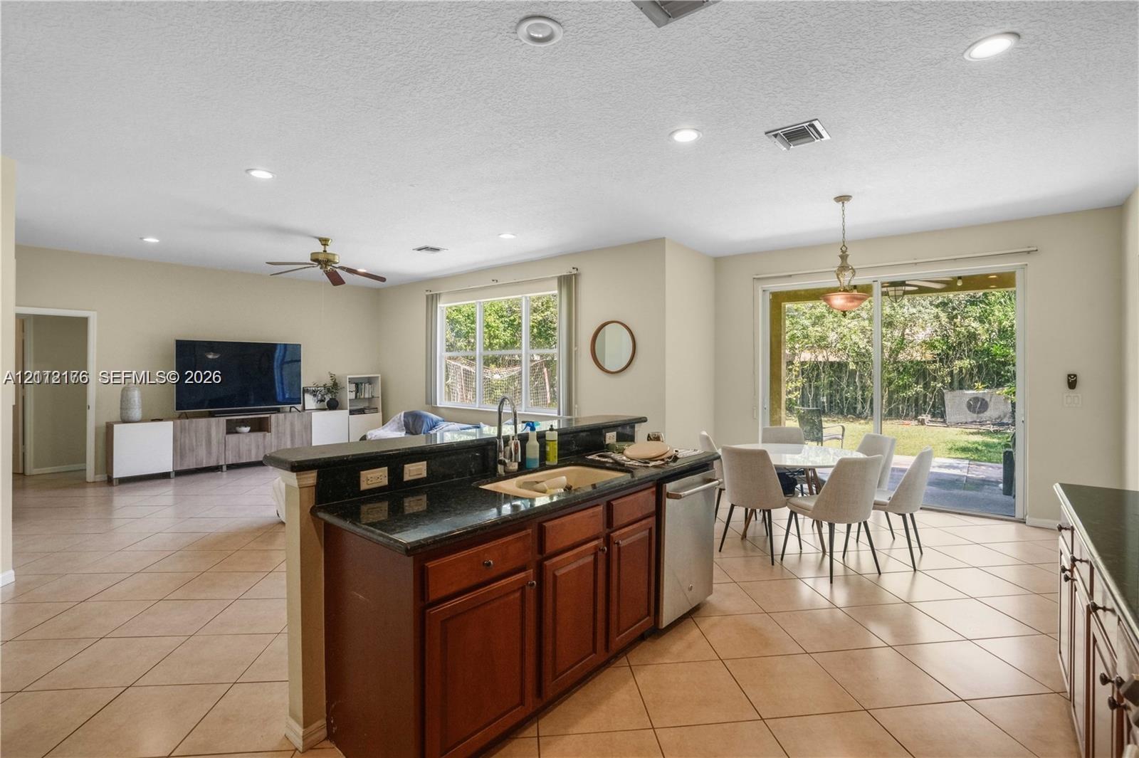 Kitchen featuring dark stone countertops, wood-finish cabinetry, stainless steel dishwasher, recessed lighting, and tile flooring