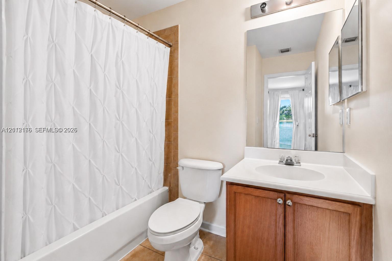 Bathroom featuring a wood-finish vanity with a solid-surface countertop, integrated basin, large wall-mounted mirror, and a tile-surround bathtub