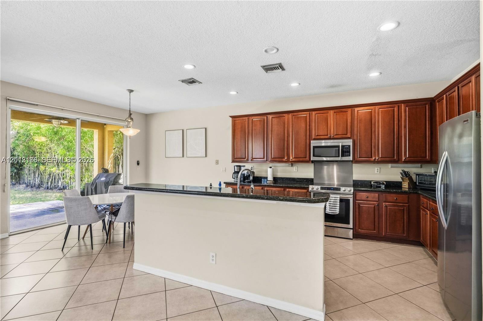 Kitchen featuring dark wood cabinetry, a breakfast bar with stone-finish countertops, stainless steel appliances, recessed lighting, and tile flooring