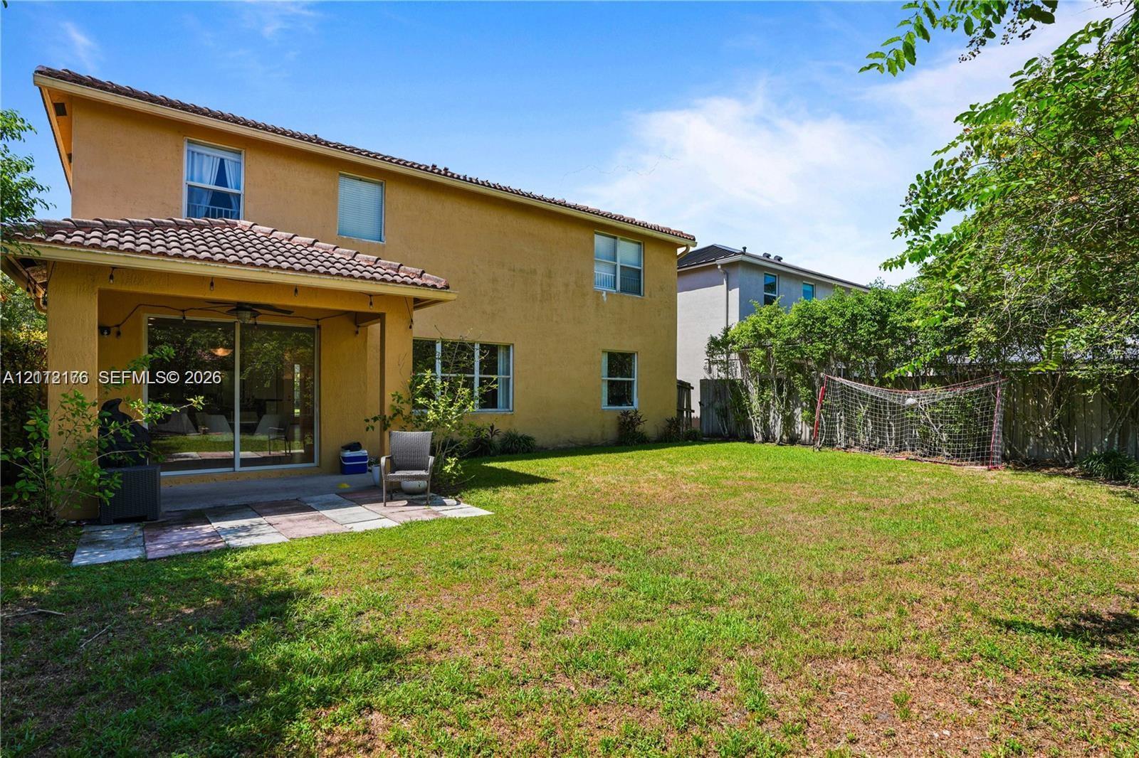 Stucco exterior with a covered patio, tile roof, and expansive backyard featuring mature perimeter landscaping