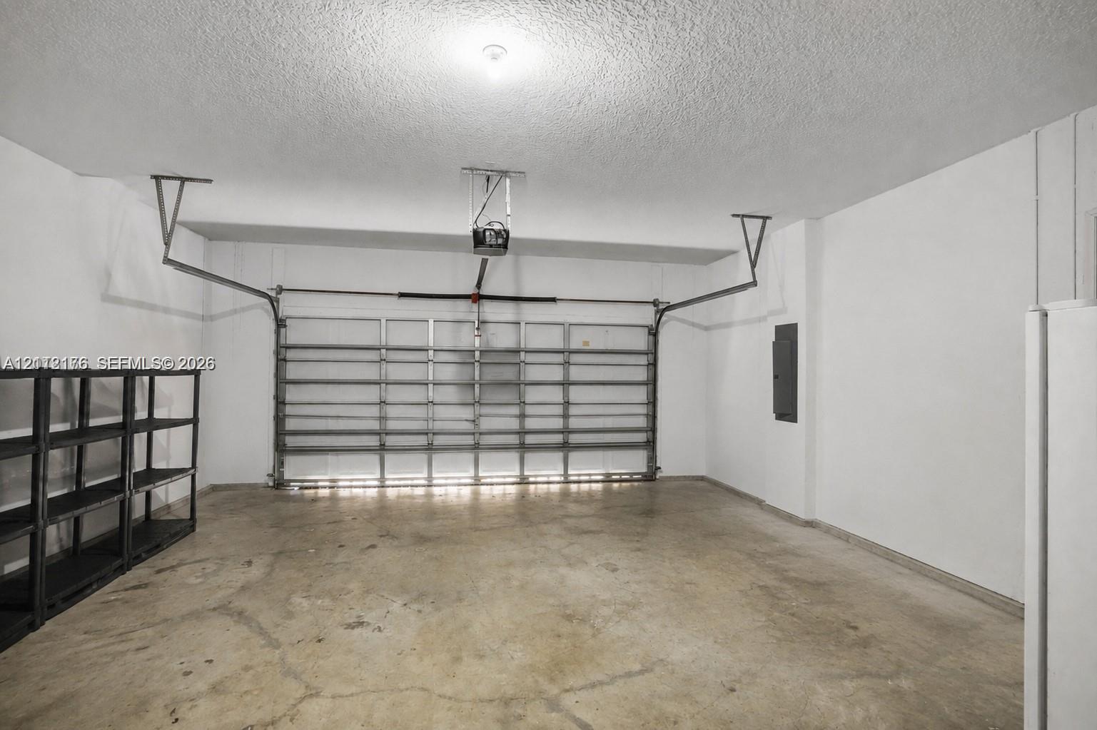 Enclosed garage featuring a concrete floor, automated door system, ceiling-mounted opener, and white walls
