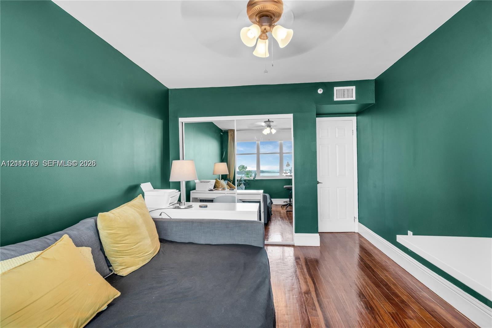 Wood-finish flooring, mirrored closet doors, and a ceiling-mounted light fixture with a fan