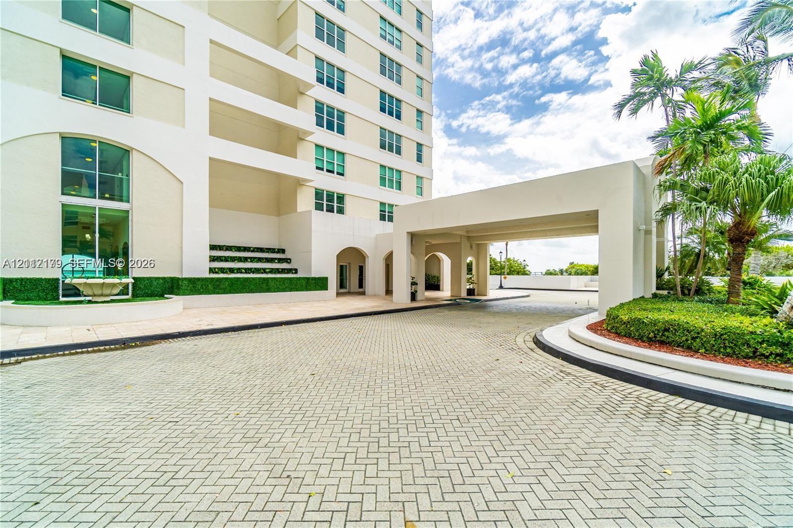Covered porte-cochre entry featuring paver hardscaping, multi-story facade with expansive glass windows, and manicured landscaping