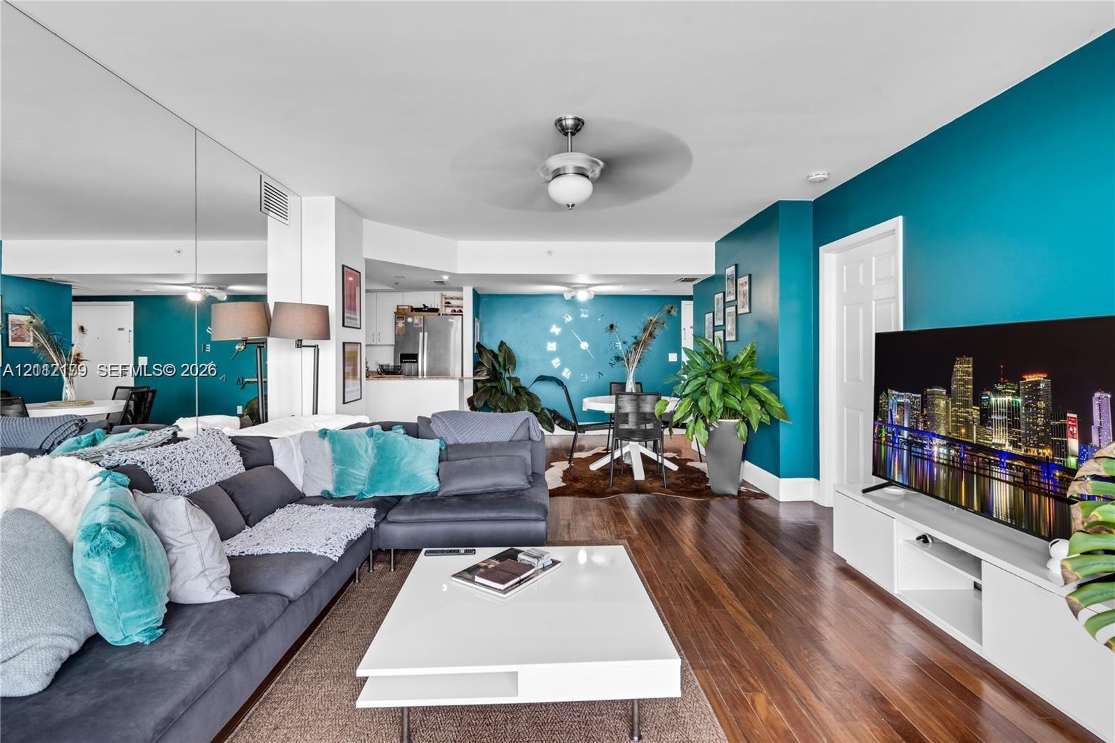 Open living area featuring wood-finish flooring, a wall-to-wall mirrored accent, ceiling fan with integrated lighting, and white built-in media cabinetry