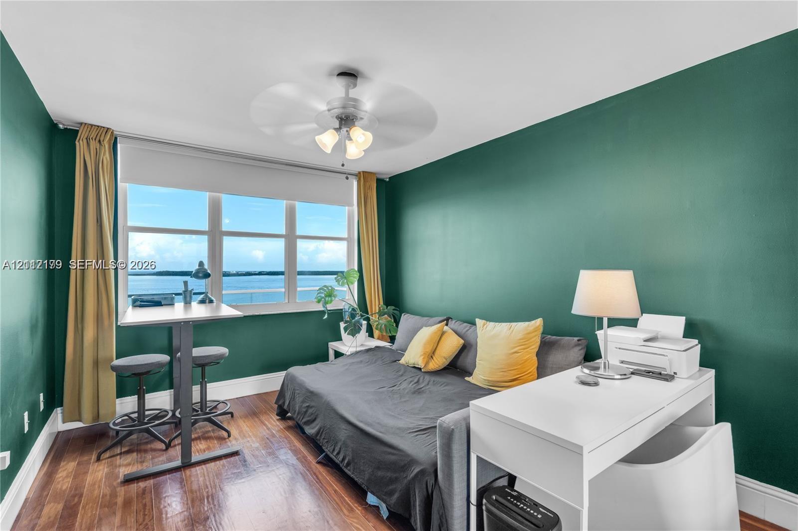 Wood-finish flooring, water-facing windows with roller shades, and a ceiling-mounted light fixture with fan