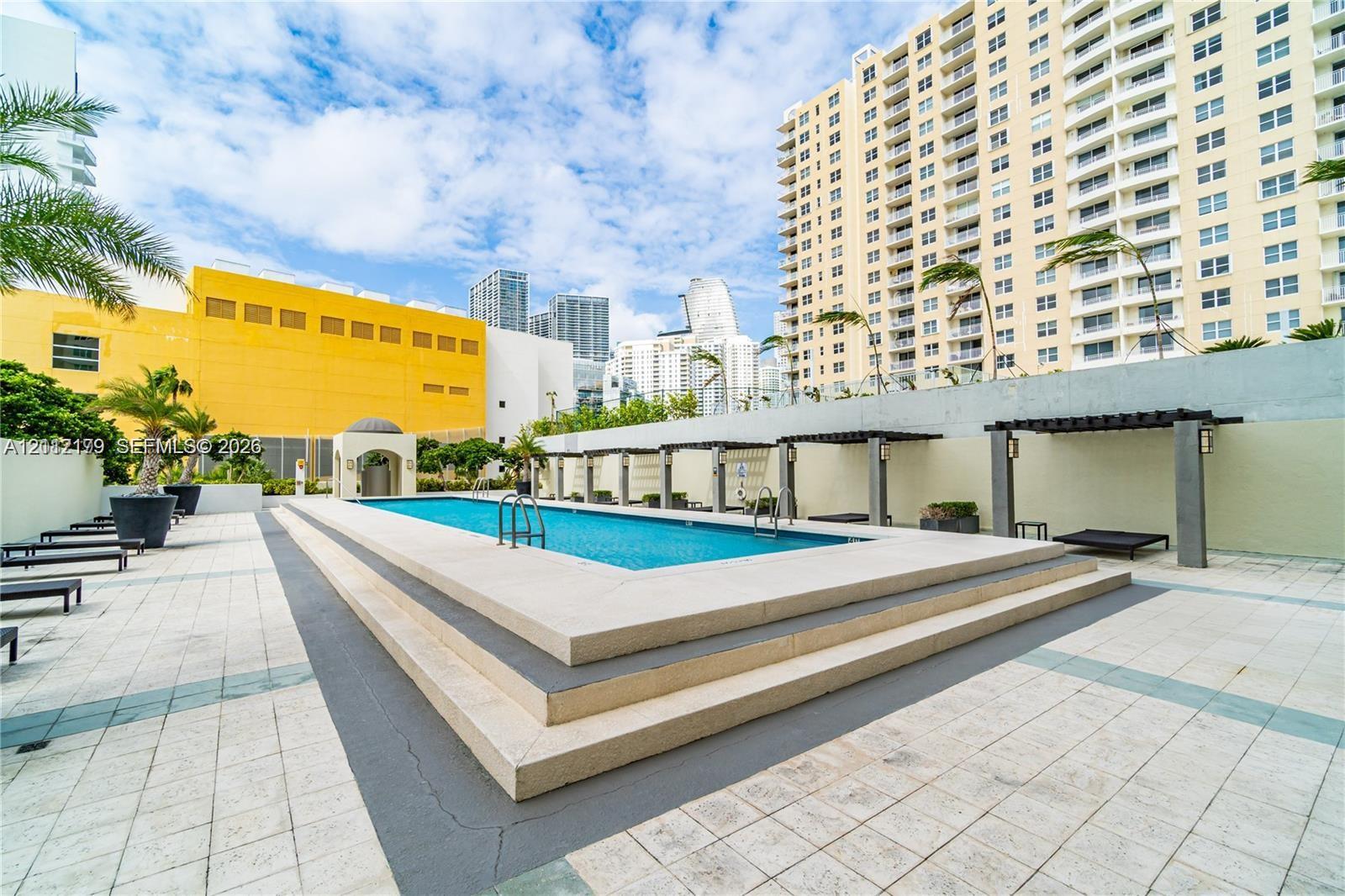 Swimming pool with stepped stone perimeter, tile decking, and built-in pergola structures