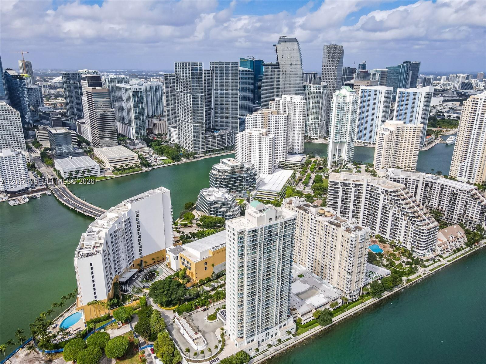 Aerial perspective of a high-density urban waterfront district featuring multiple high-rise structures, inland waterways, a bridge, and surrounding coastal infrastructure