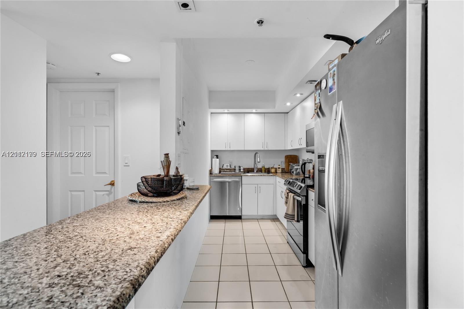 Kitchen featuring white cabinetry, stone-surface breakfast bar, ceramic tile flooring, stainless steel appliances, and recessed lighting