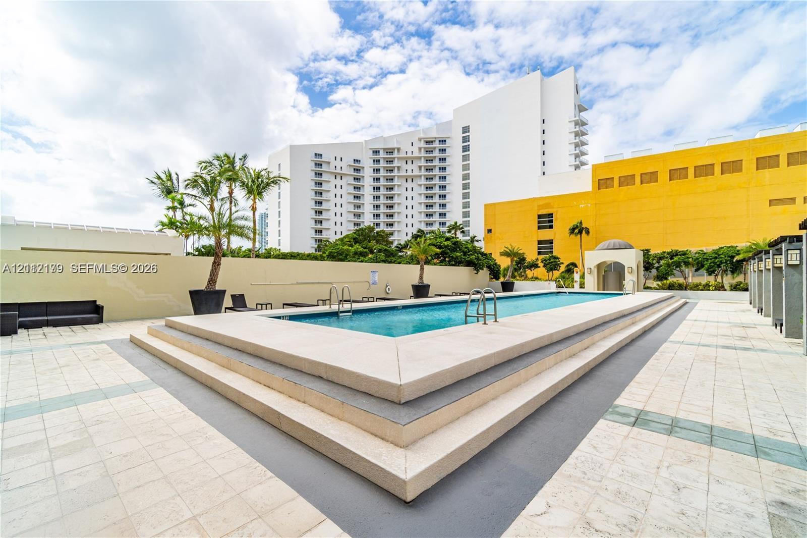 Elevated rectangular swimming pool featuring tiered concrete steps, perimeter coping, and metal entry ladders, set within a tiled deck