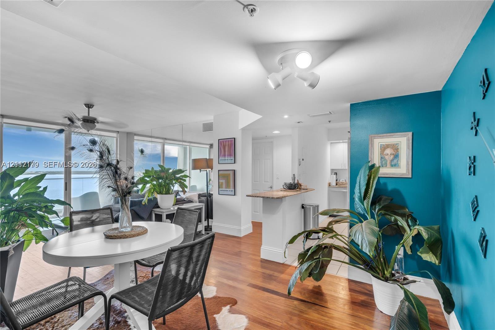 Interior space featuring wood-finish flooring, floor-to-ceiling sliding glass doors, a built-in peninsula with a stone-finish countertop, and multi-directional ceiling-mounted track lighting Interior space featuring wood-finish flooring, floor-to-ceiling sliding glass doors, a built-in peninsula with a stone-finish countertop, and multi-directional ceiling-mounted track lighting