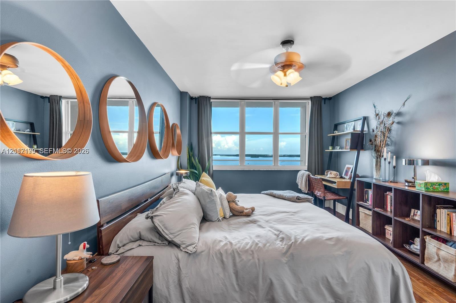 Multi-panel window with water backdrop, wood-finish flooring, and ceiling fan with integrated lighting