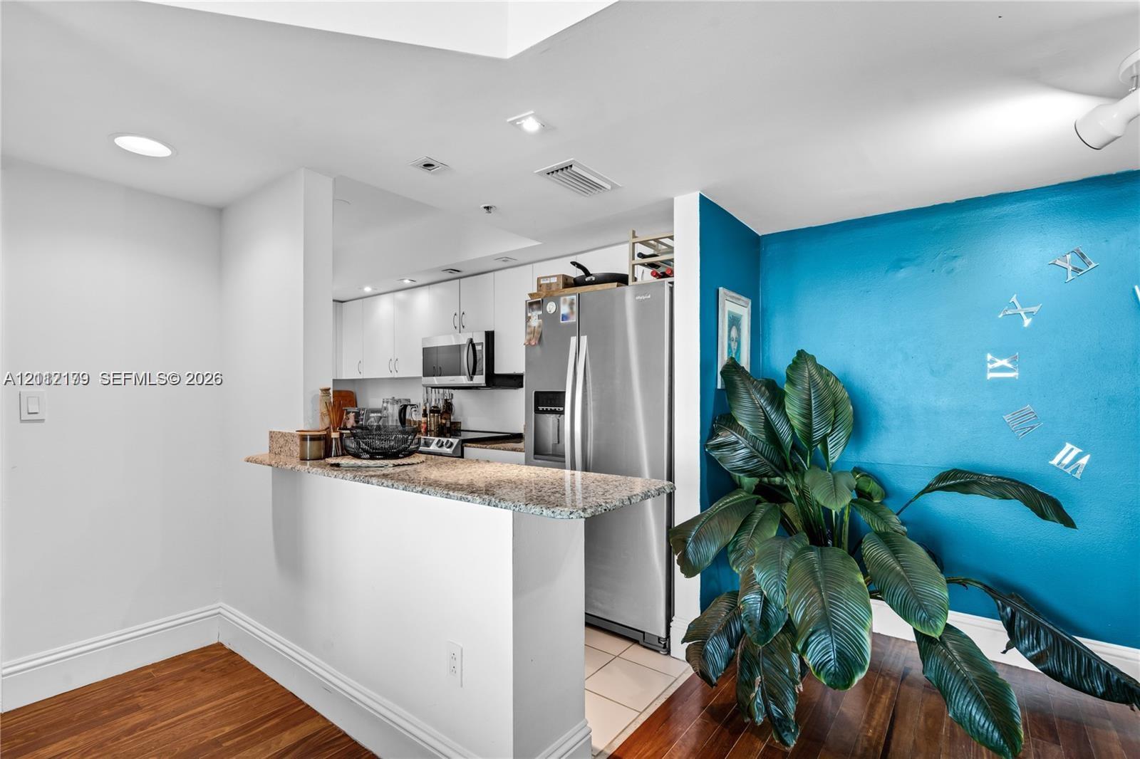 Kitchen featuring white cabinetry, stone-surface breakfast bar, stainless steel refrigerator, built-in microwave, and wood-finish flooring