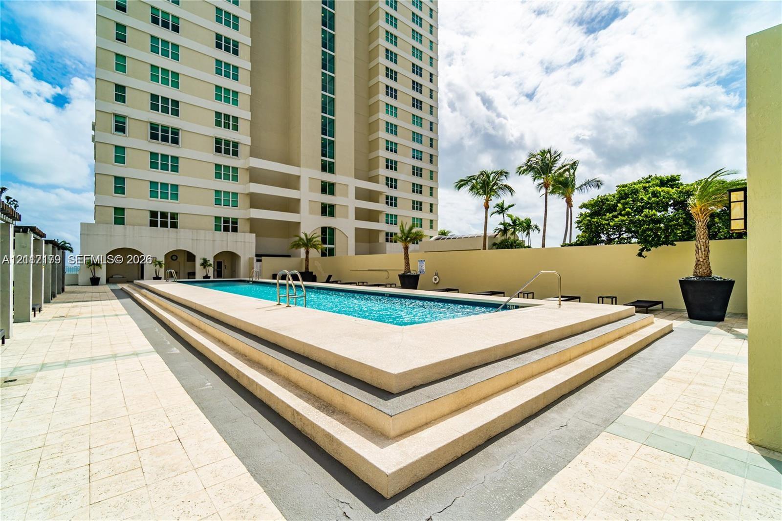 Elevated swimming pool featuring a stepped concrete surround, tile-finished pool deck, and palm tree landscaping
