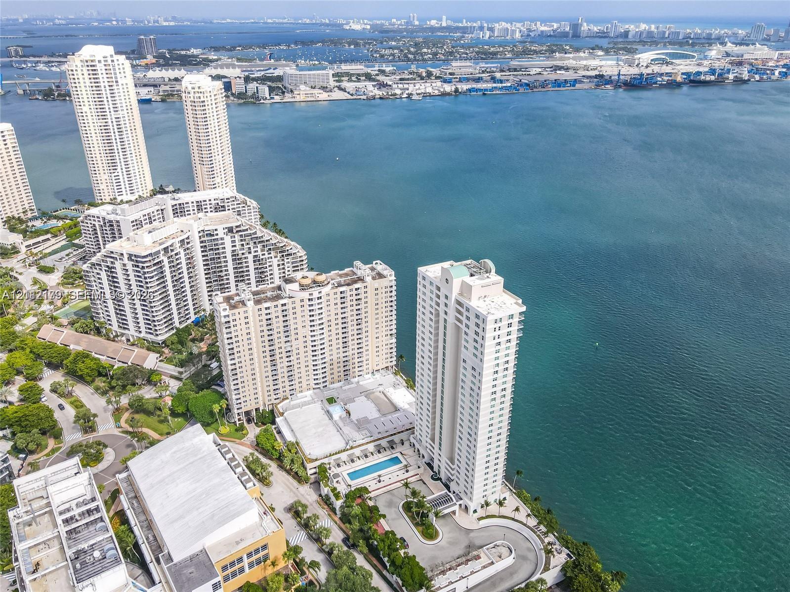 Aerial perspective of the high-rise structure featuring an outdoor swimming pool, paved motor court, mature landscaping, and waterfront positioning