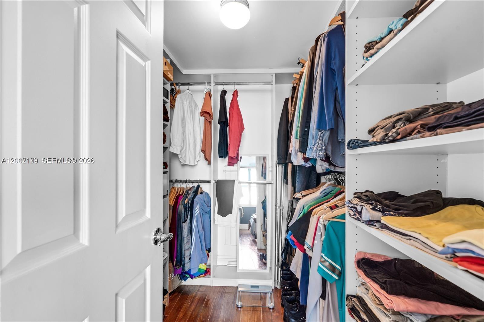 Walk-in closet featuring white built-in shelving, adjustable storage units, integrated hanging rods, and wood-finish flooring