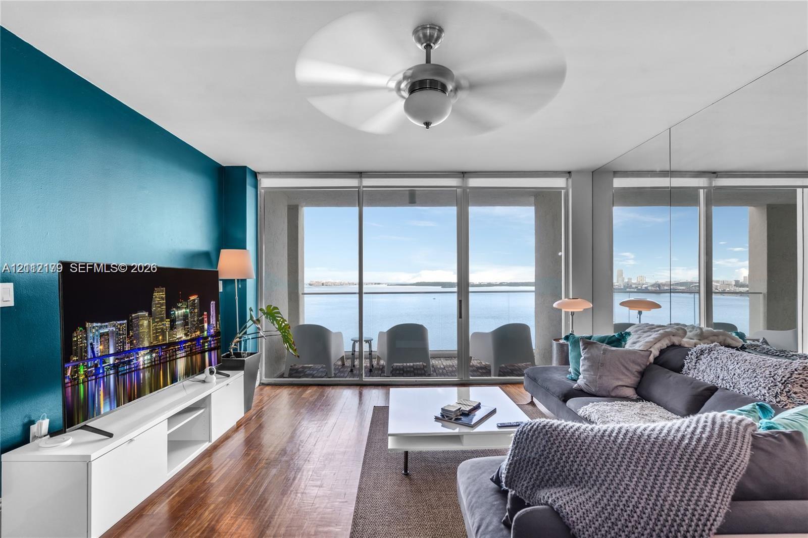 Floor-to-ceiling sliding glass doors, full-wall mirror, wood-finish flooring, ceiling fan, and direct water horizon
