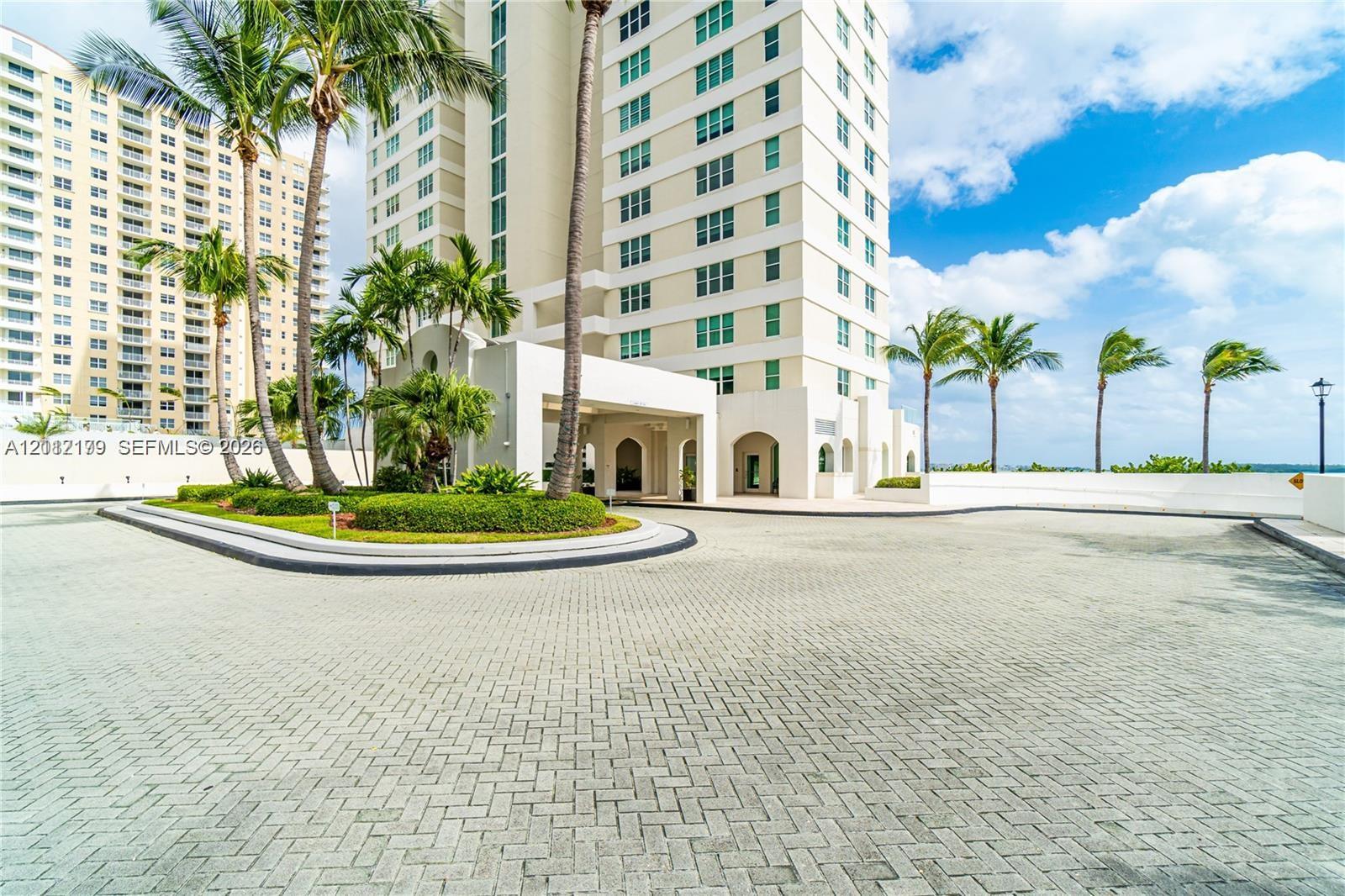 High-rise exterior featuring a paved arrival courtyard, porte-cochre, mature palm trees, and manicured landscaping