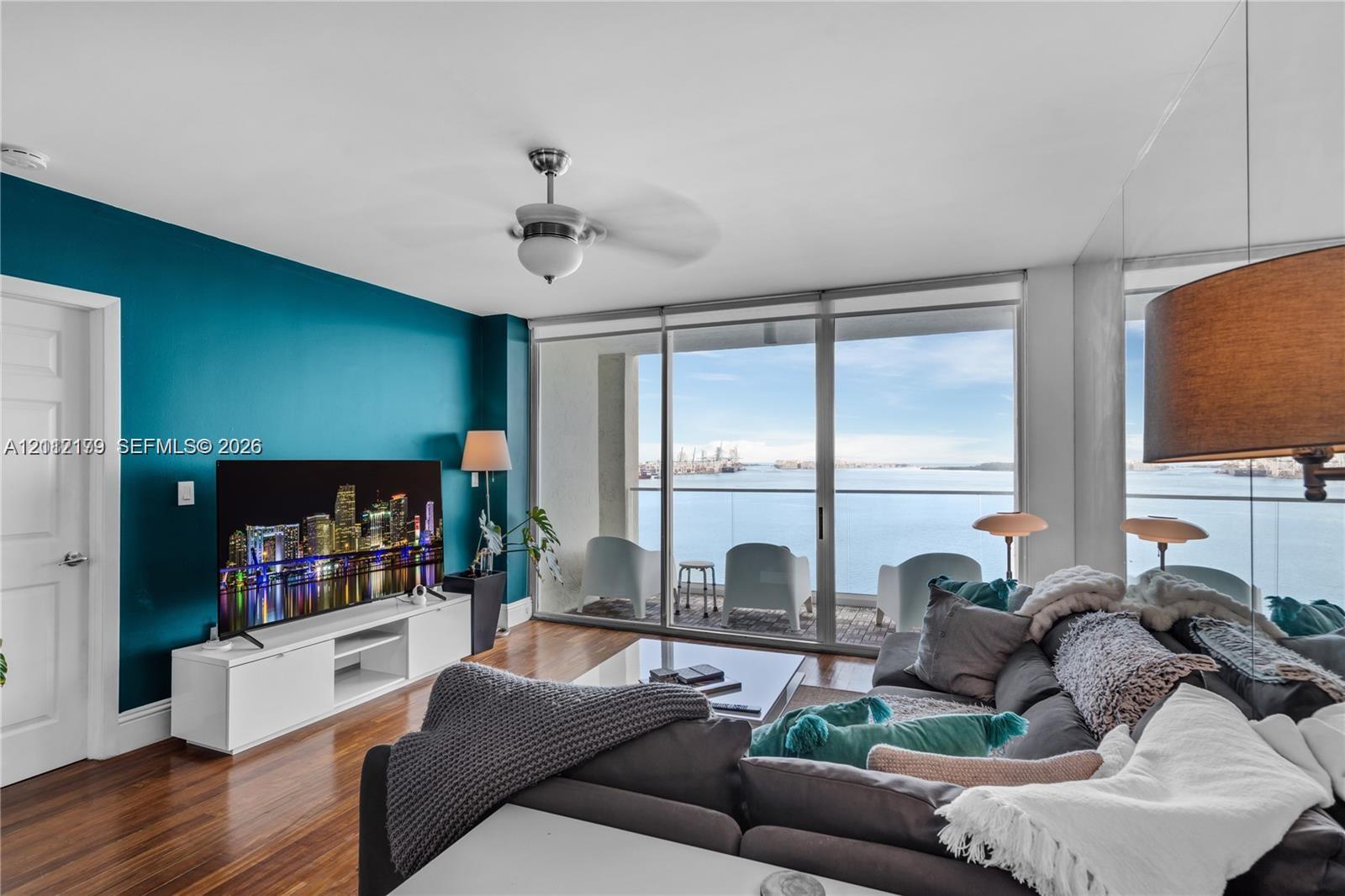 Living space featuring floor-to-ceiling glass sliding doors, wood-finish flooring, a ceiling fan with integrated light fixture, and a mirrored wall panel