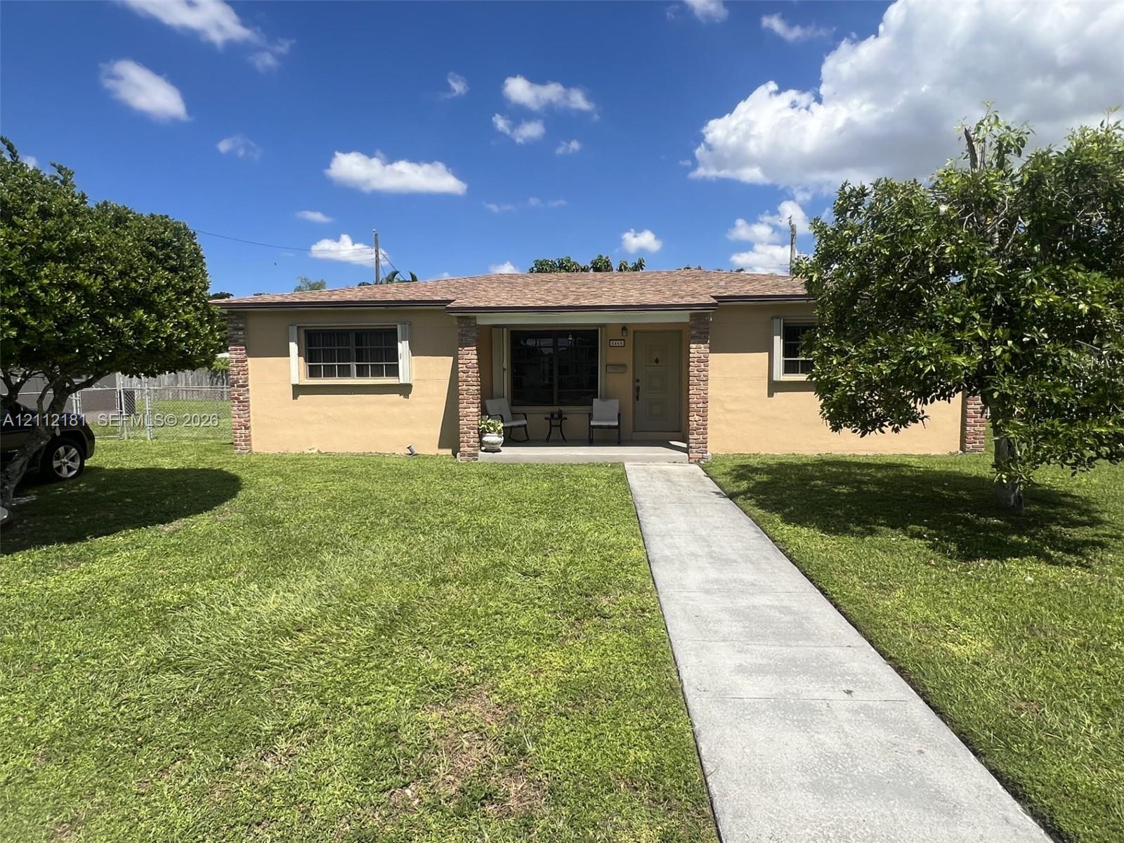 Single-story exterior featuring a stucco facade, brick-accented entryway, composition shingle roof, concrete front walkway, and mature landscaping