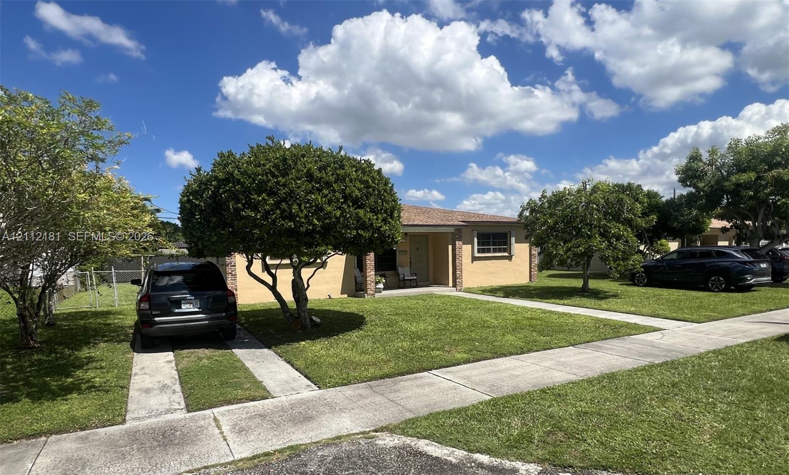 Single-story masonry exterior featuring a concrete ribbon driveway, expansive front lawn, mature shade trees, and a recessed entryway