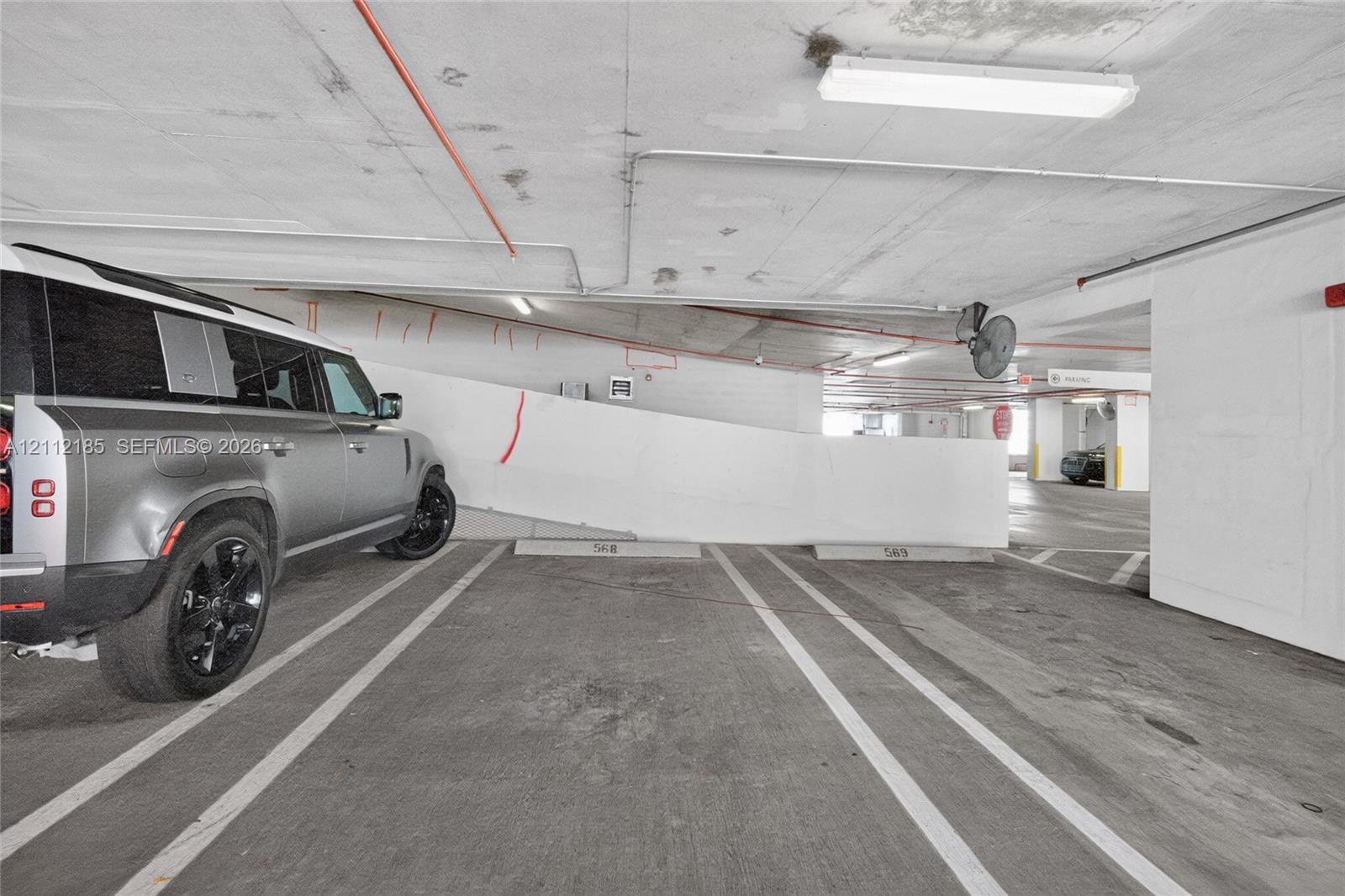 Covered parking facility with concrete flooring, designated stalls, and overhead industrial lighting