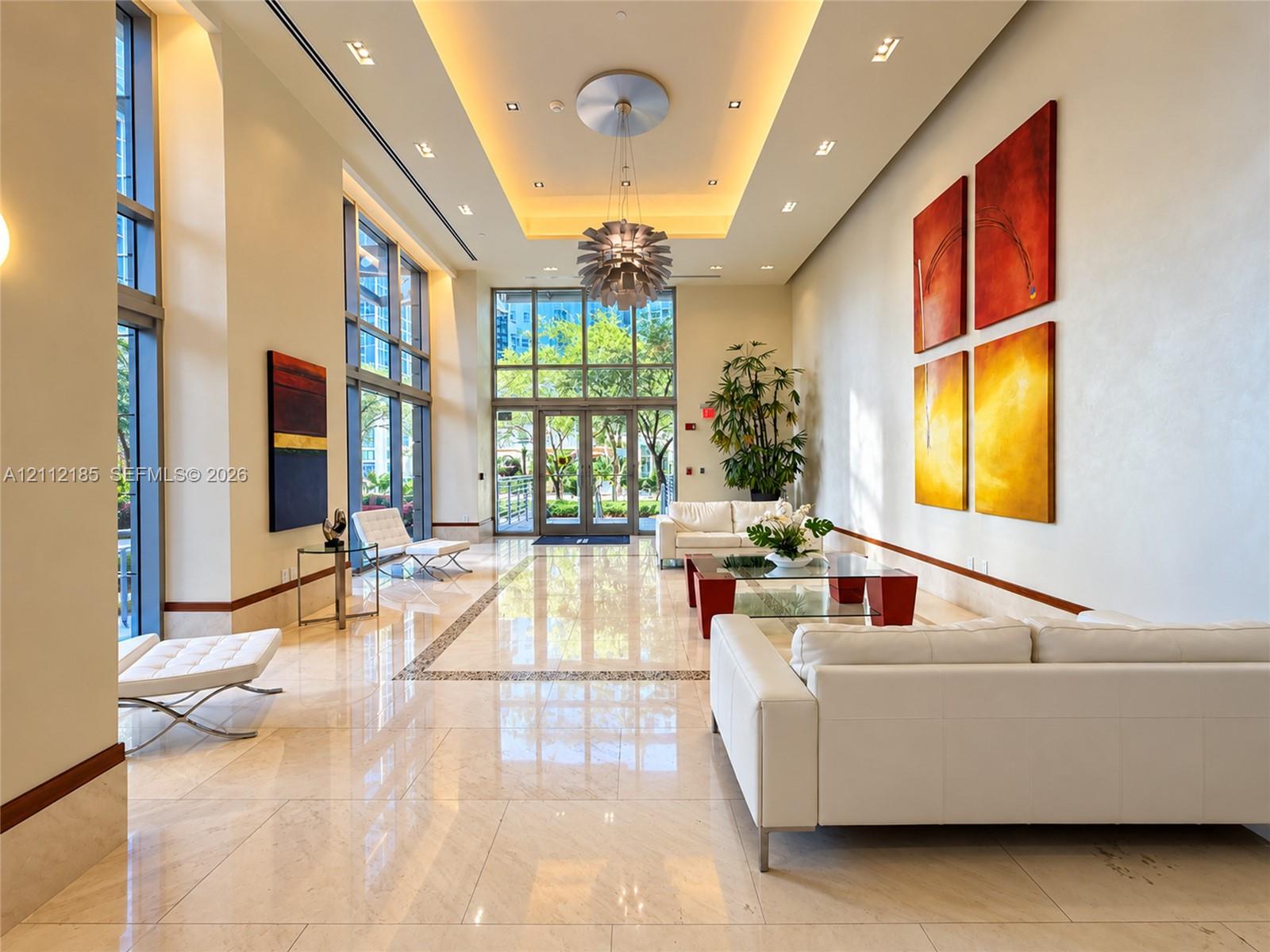 Expansive lobby featuring polished stone flooring, floor-to-ceiling windows, recessed cove lighting, and a modern sculptural chandelier