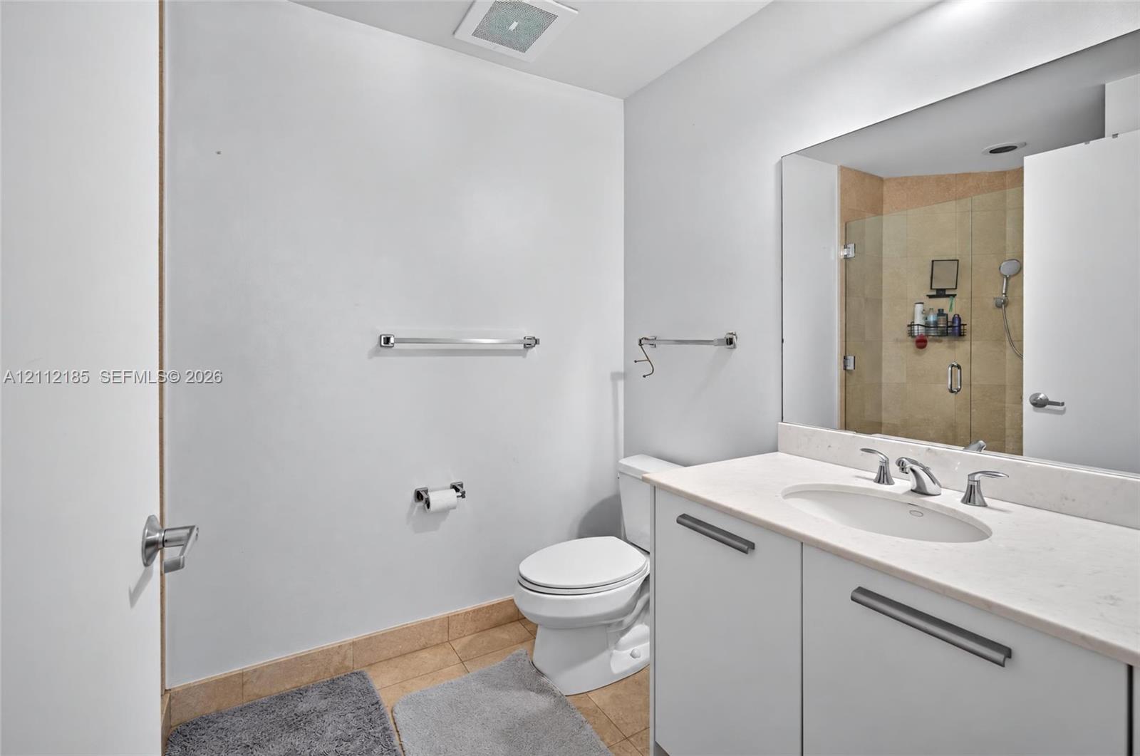 Bathroom featuring a white vanity with a stone countertop and undermount sink, large wall-mounted mirror, and a glass-enclosed shower with stone tile surround