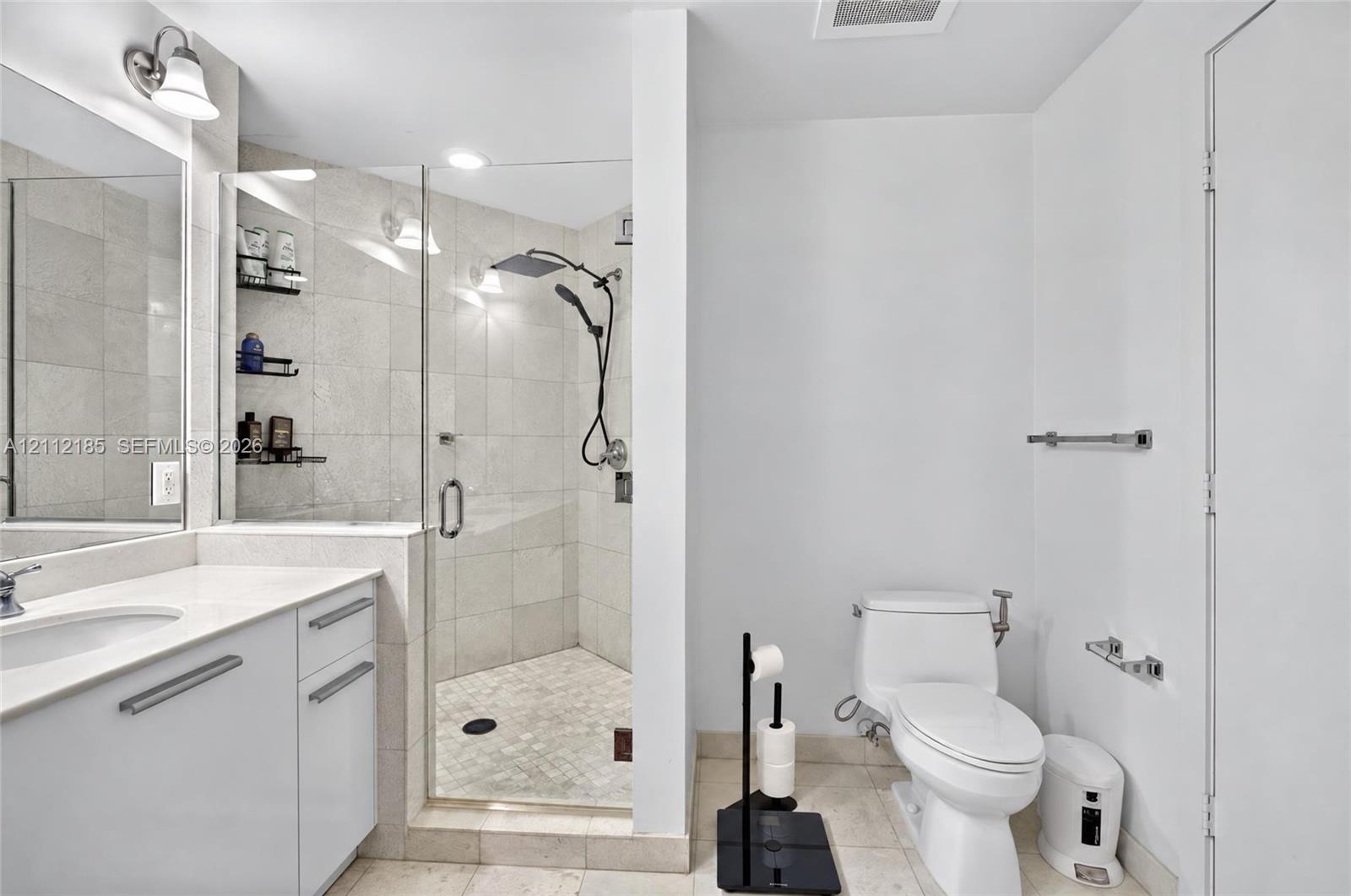 Bathroom featuring a white vanity with a composite countertop, an integrated sink, a glass-enclosed shower with tile surround, a rainfall showerhead, and recessed lighting
