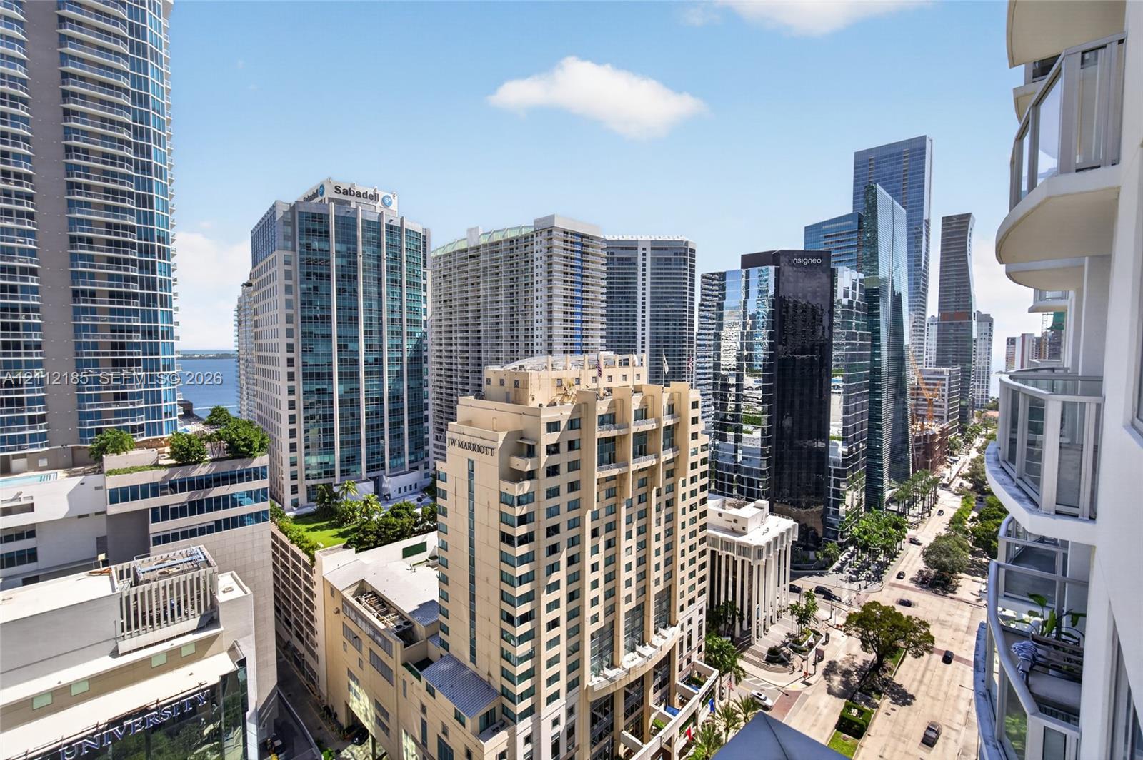 High-rise balcony with glass railings overlooking a dense urban cityscape featuring multiple skyscraper structures and street-level thoroughfares