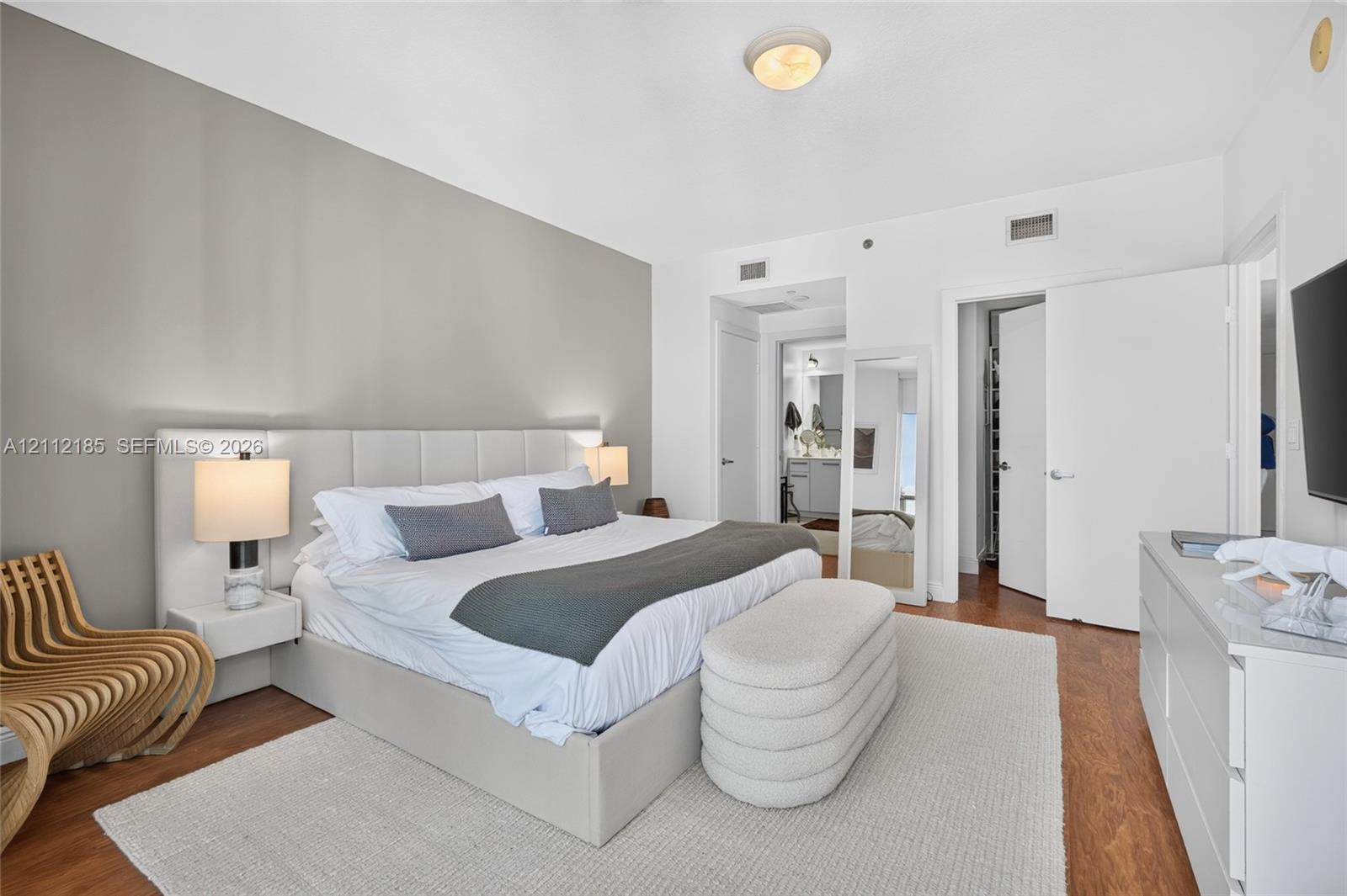 Neutral-toned room featuring wood-finish flooring, a contemporary floating headboard with integrated side tables, and multiple interior door access points