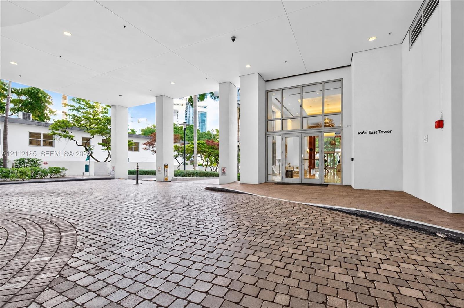 Covered motor court entrance featuring stone paver driveway, glass-paneled double entry doors, high ceilings with recessed lighting, and support columns
