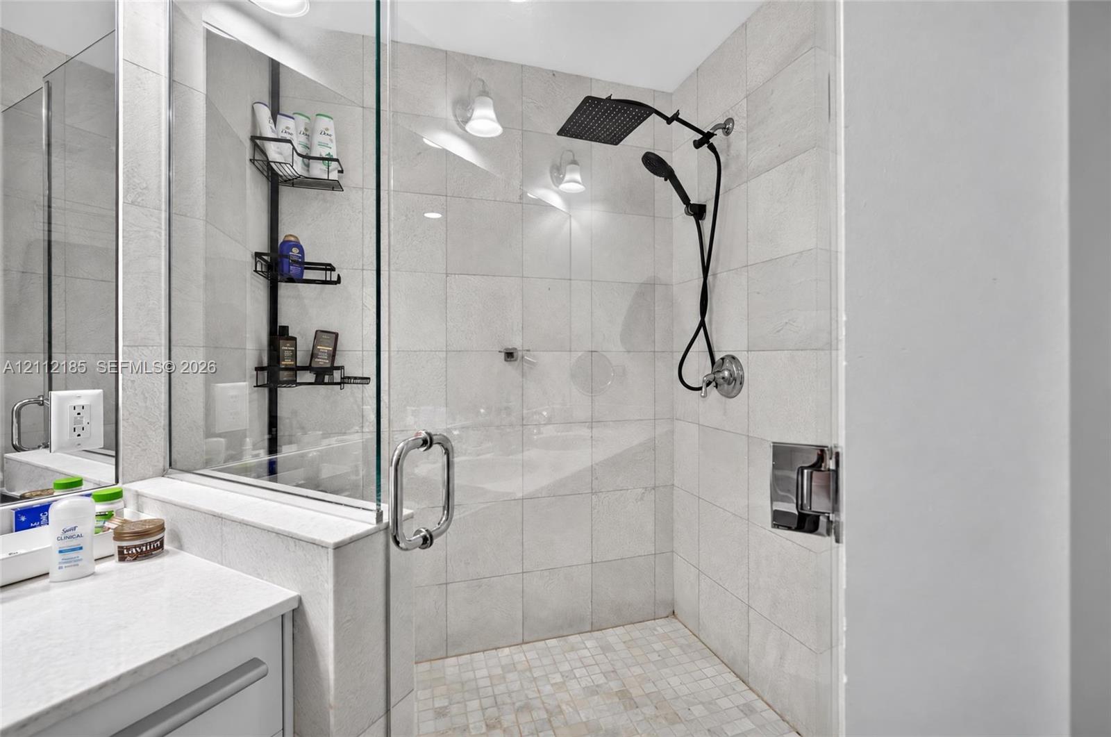 Walk-in shower featuring light-toned tile wall surround, mosaic tile floor, glass enclosure, and dual-function matte black showerhead