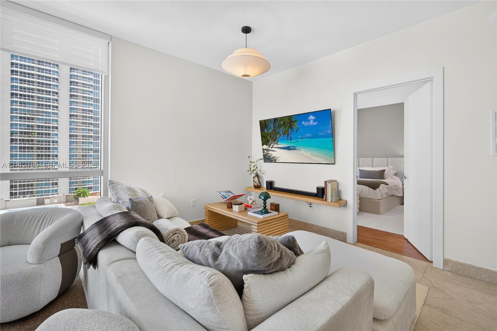 Large floor-to-ceiling windows, wall-mounted natural wood floating shelf, semi-flush mount pendant lighting, and neutral stone-finish flooring