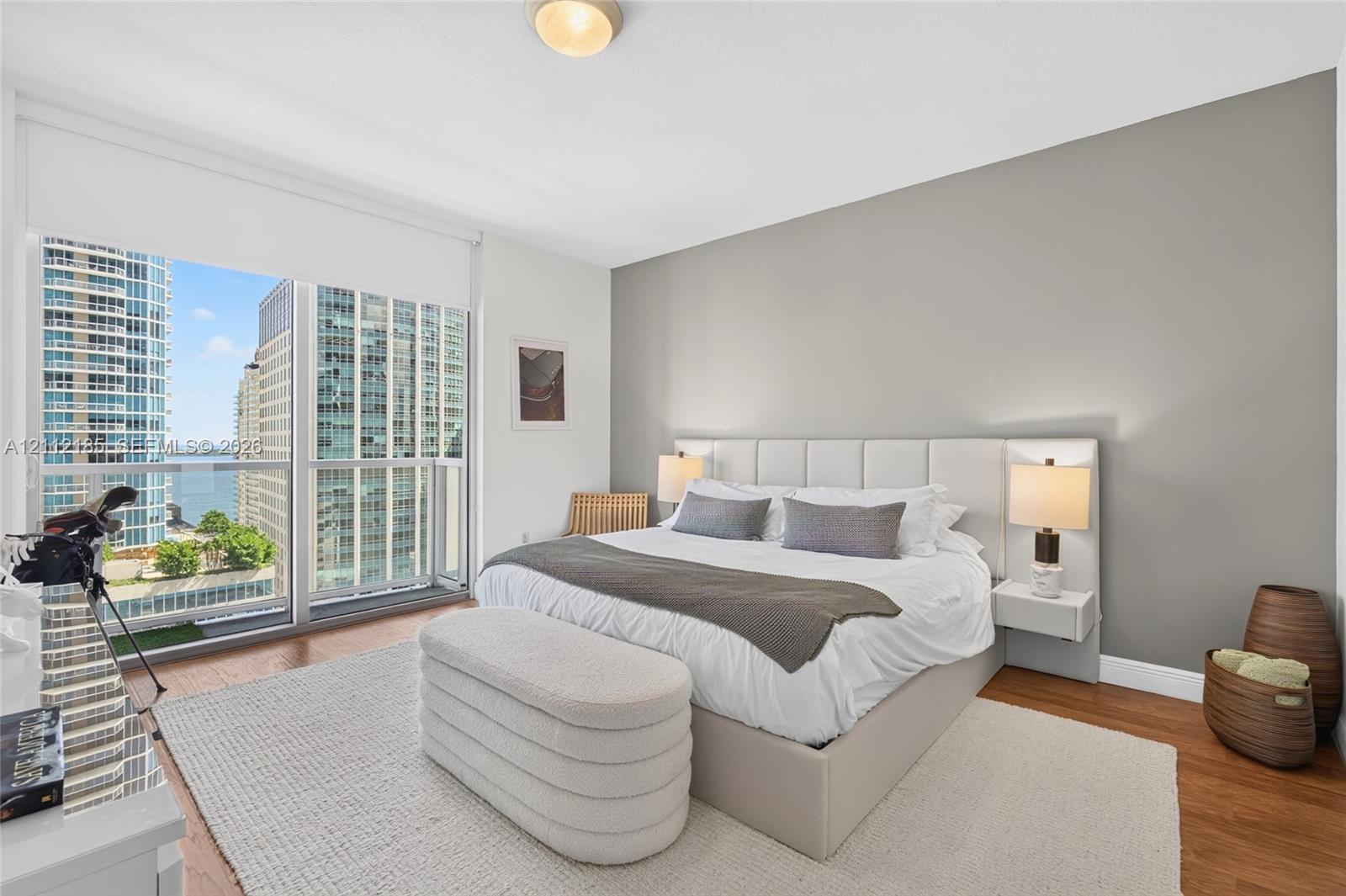 Bedroom featuring floor-to-ceiling windows, wood-finish flooring, a neutral accent wall, and a custom built-in headboard with integrated floating nightstands