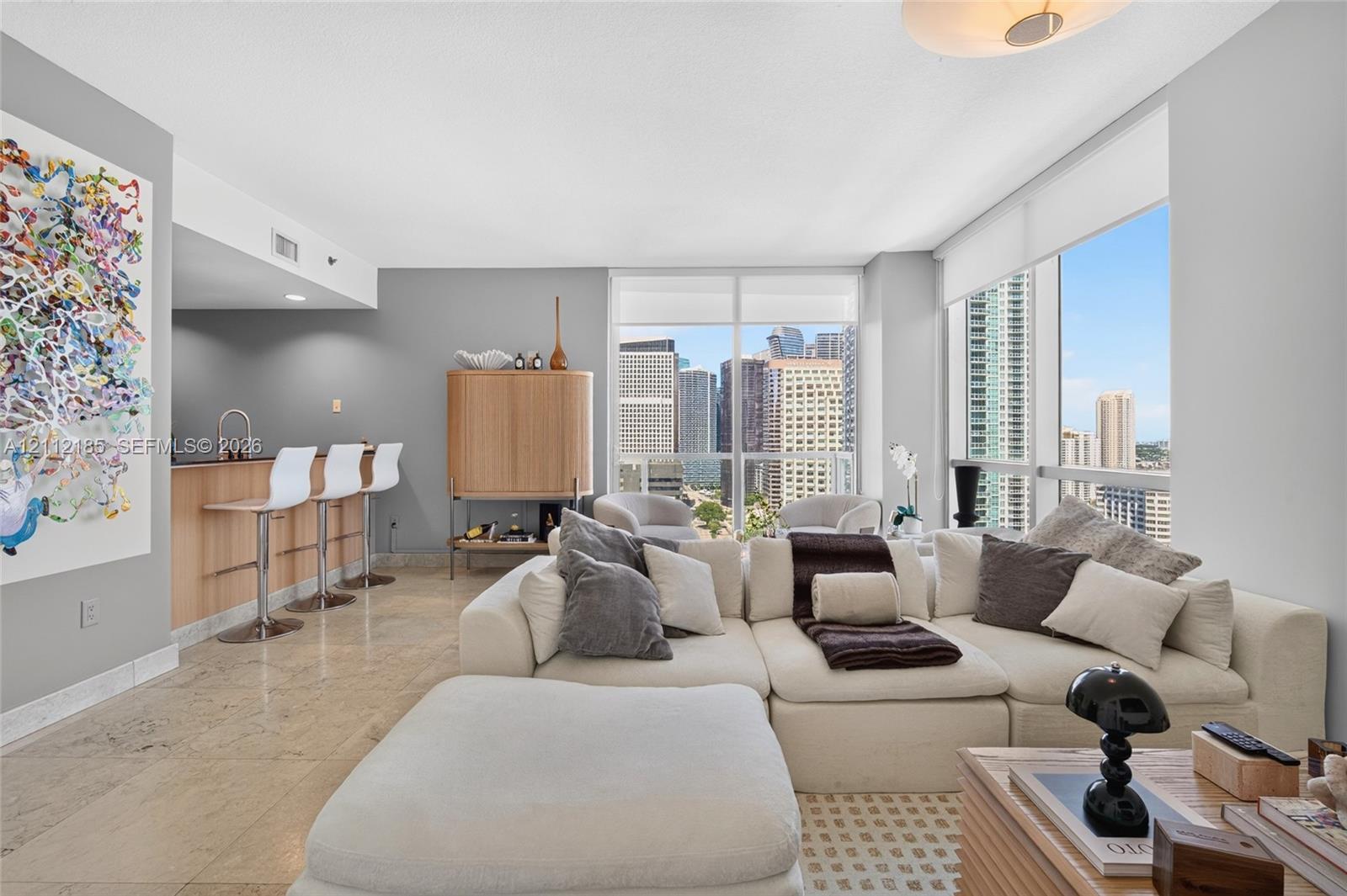 Open-concept living area featuring stone flooring, floor-to-ceiling windows, and a built-in kitchen island with a sink and faucet