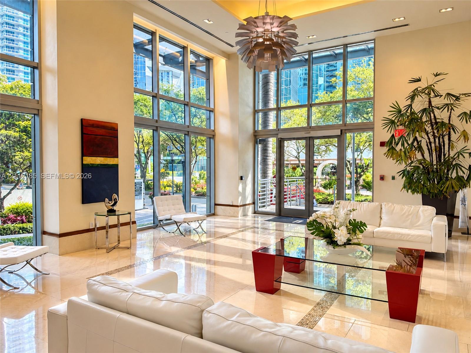 Double-height lobby featuring floor-to-ceiling glass windows, recessed ceiling lighting, polished stone flooring, and a decorative modern pendant chandelier