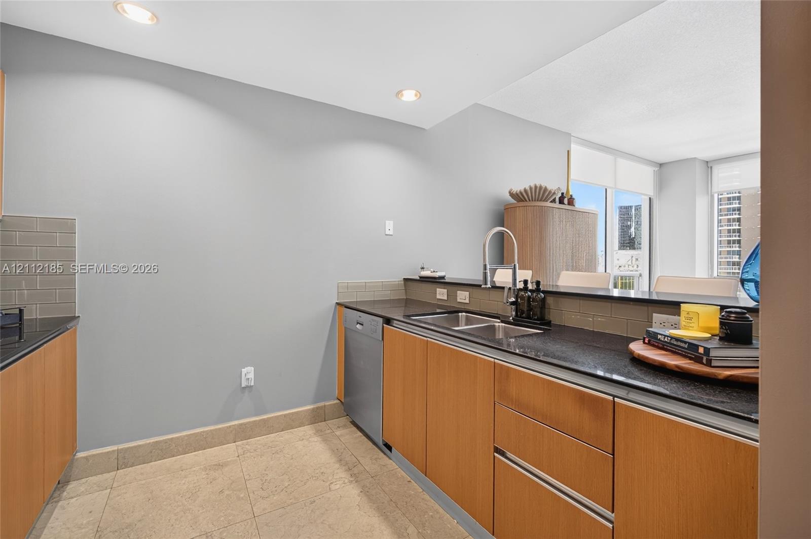 Kitchen featuring flat-panel wood cabinetry, dark stone countertops, an undermount double-basin sink with a high-arch faucet, integrated dishwasher, and tile backsplash