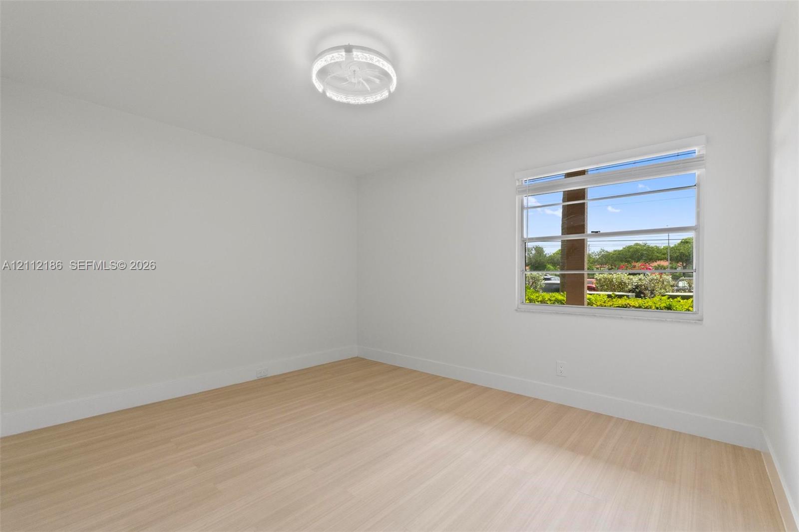 Light-filled room featuring wood-finish flooring, crisp neutral walls, and a modern circular LED flush-mount fixture