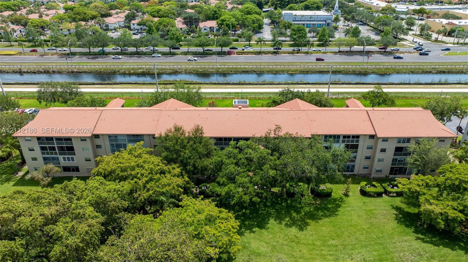 Multi-story building featuring a tile roof, screened-in balcony enclosures, and expansive surrounding green space with mature trees