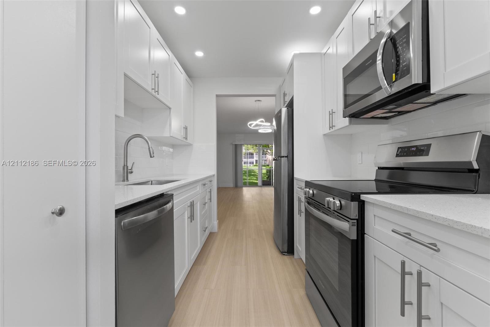 Kitchen featuring white shaker-style cabinetry, stainless steel appliances, quartz countertops, tile backsplash, and wood-finish flooring