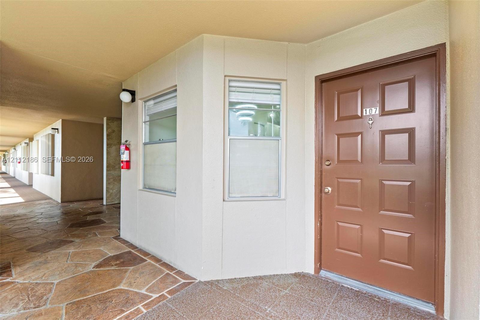 Entrance featuring a solid-core raised panel door, stone-finish exterior flooring, and double-hung windows