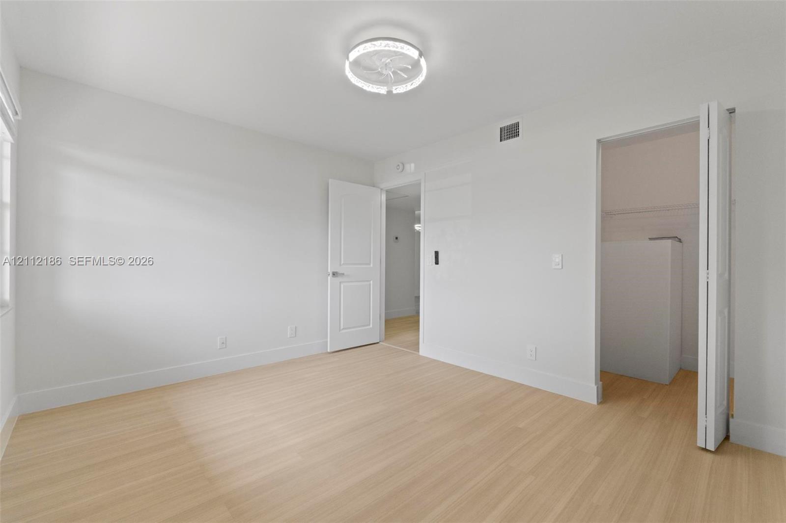Light-toned wood-finish flooring, crisp neutral wall paint, modern ceiling-mounted lighting fixture, and interior doors with integrated closets