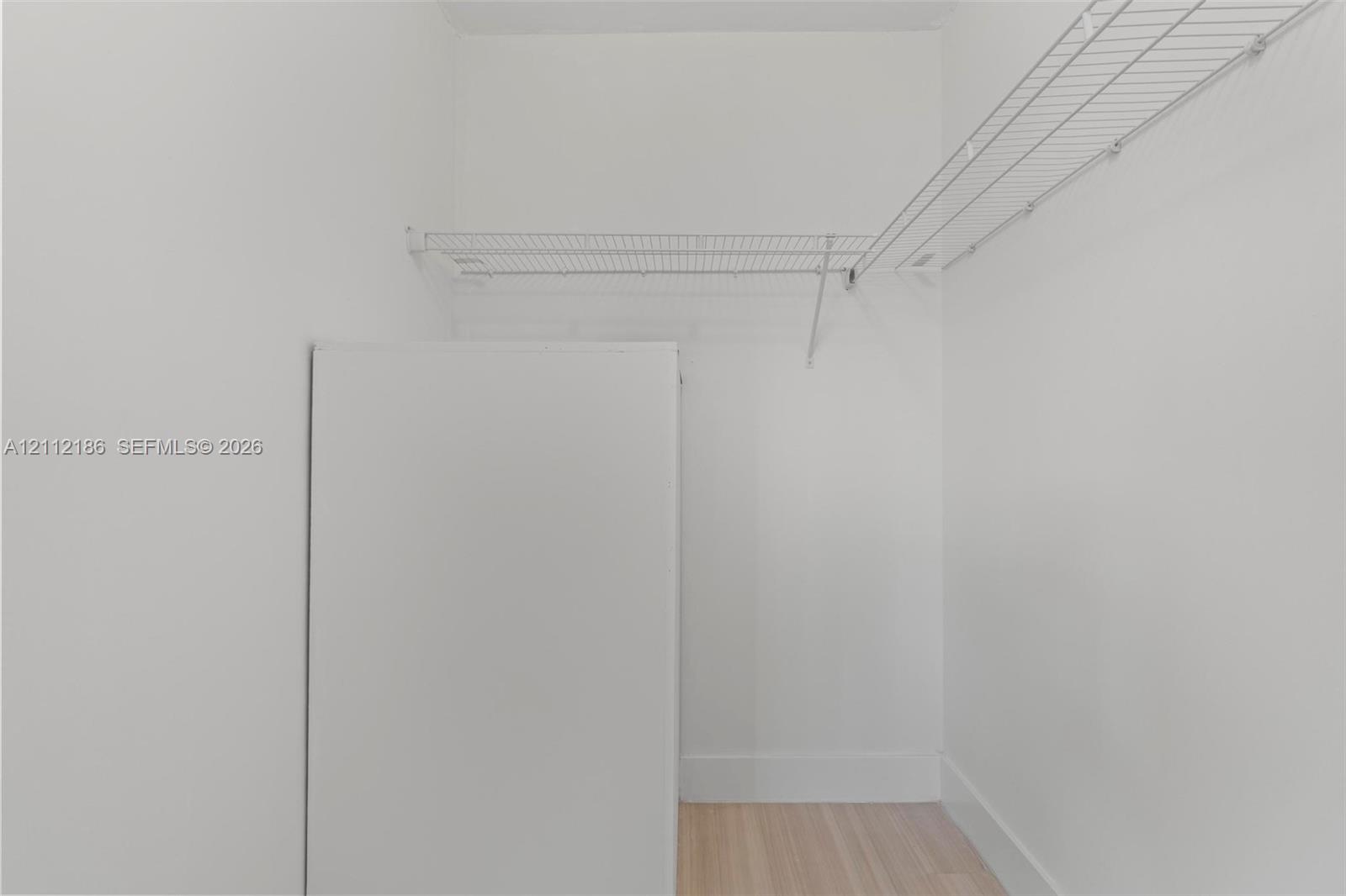 Storage area featuring white walls, wood-finish flooring, and integrated white wire shelving