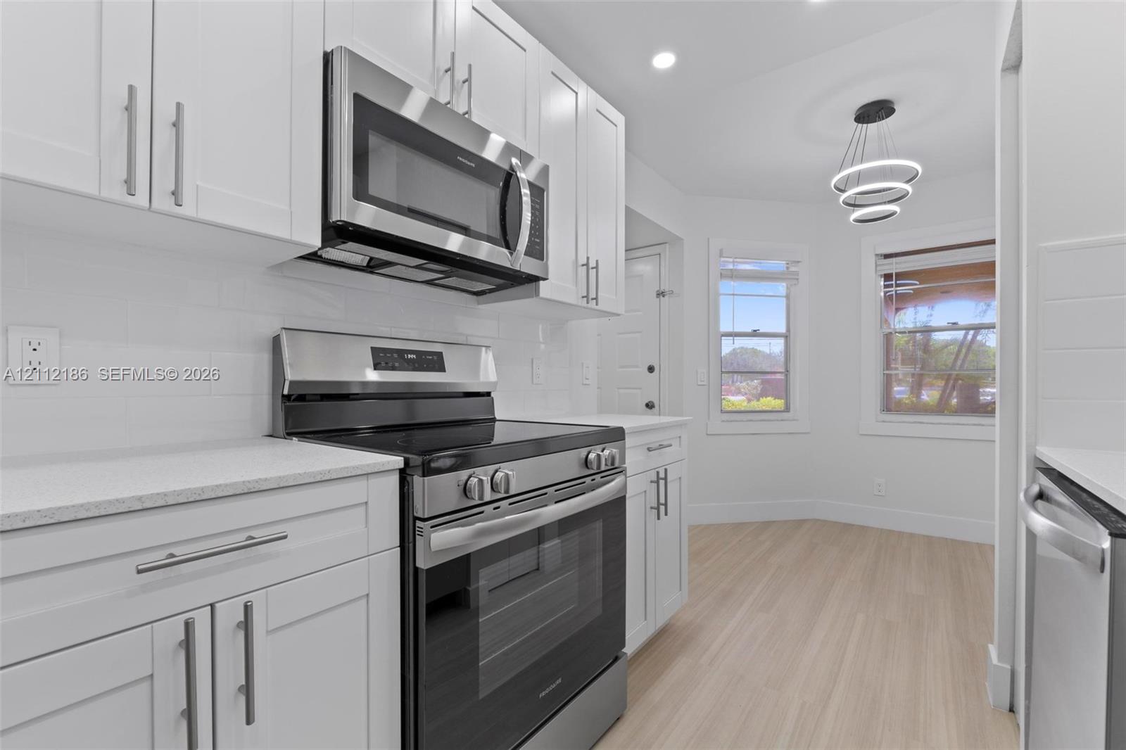 Kitchen featuring white shaker-style cabinetry, stainless steel appliances, light-toned stone countertops, subway tile backsplash, and tiered pendant lighting
