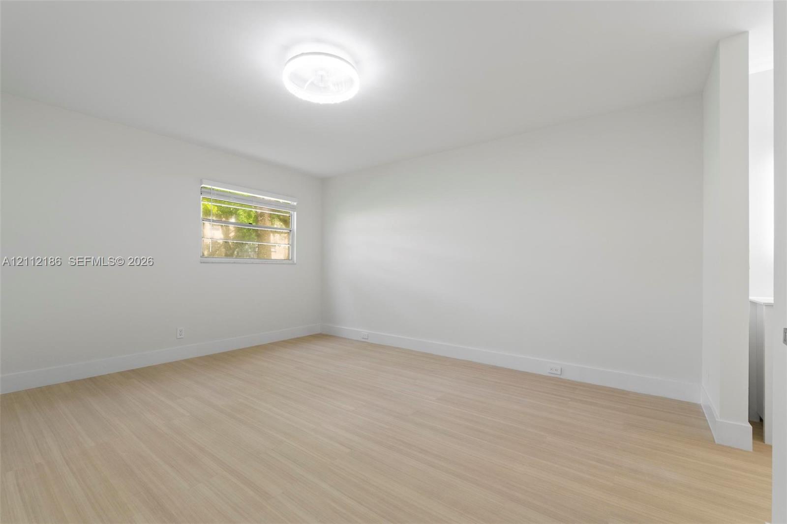 Interior room featuring light-toned wood-finish flooring, neutral walls, a single-pane window, and a flush-mount circular ceiling fixture
