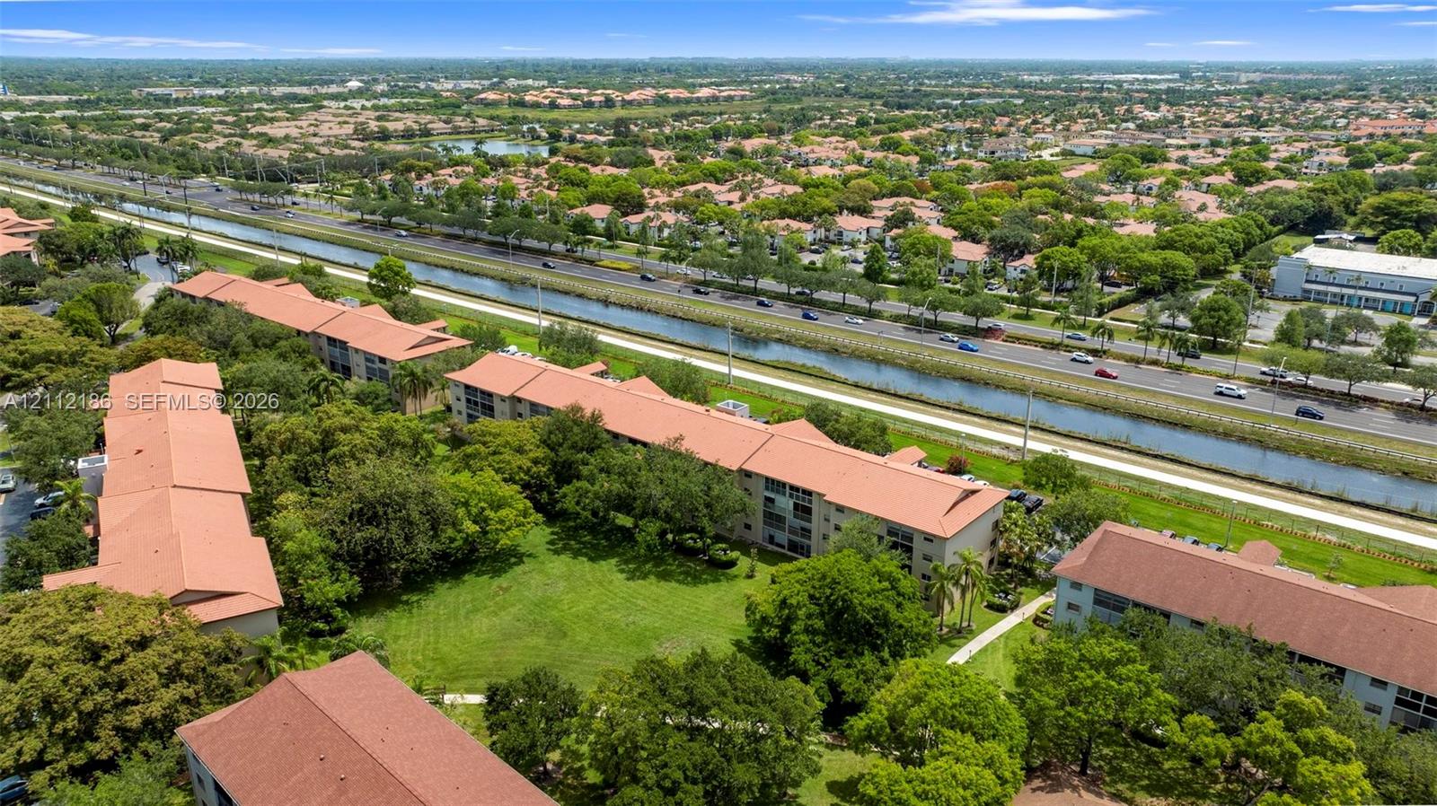 Aerial perspective of multi-story buildings with terracotta-style roof tiles, featuring landscaped grounds, mature trees, and pedestrian pathways