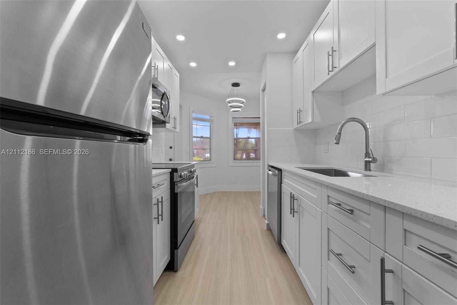 Kitchen featuring white shaker-style cabinetry, quartz countertops, stainless steel appliances, white subway tile backsplash, and light-toned wood-finish flooring