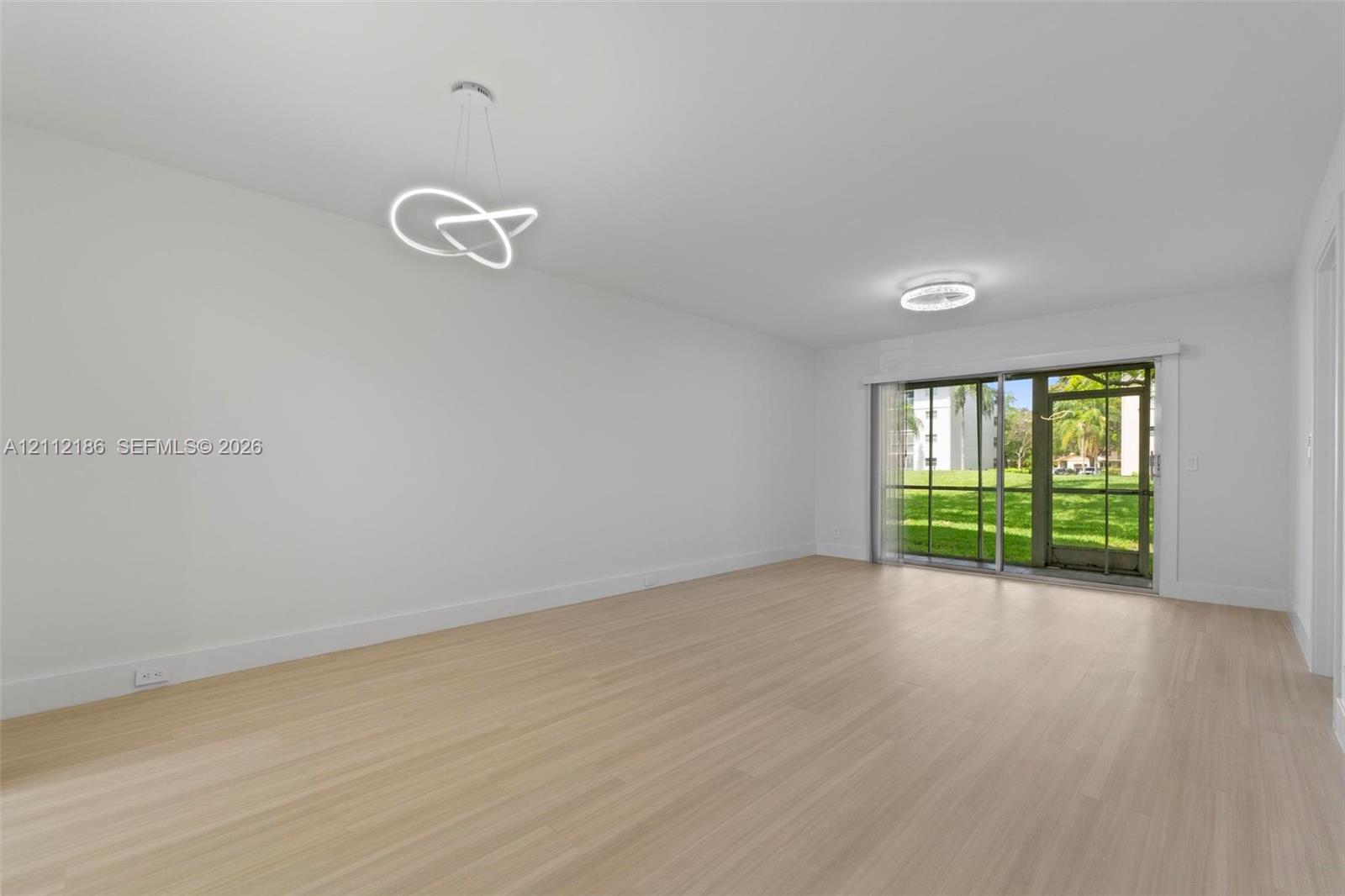 Open-concept interior featuring light wood-finish flooring, modern geometric LED pendant lighting, and a sliding glass door providing external access